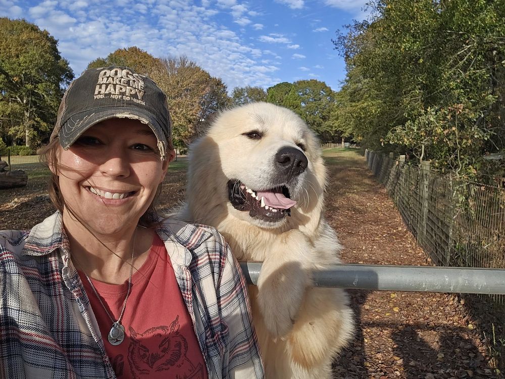 Jenn smiling outdoors beside her white dog, Ted E. Bear